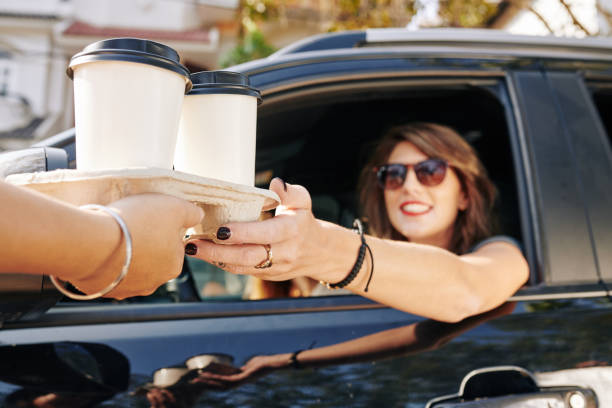 Waiter giving disposable tray with two cups of take out coffee to pretty smiling female driver